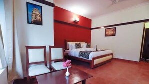 A hotel room with a bed, two chairs, a table, and a vase of flowers. - Maya The Forest Resort (Ramnagar)