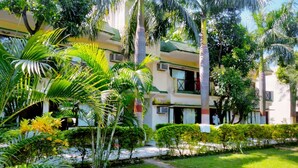 A multi-story building with a green roof, surrounded by lush greenery and palm trees. - Maya The Forest Resort (Ramnagar)