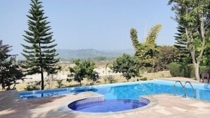 A swimming pool with a hot tub, surrounded by trees and a view of distant hills. - Maya The Forest Resort (Ramnagar)