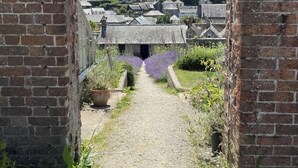 Un arco de ladrillo que da paso a un sendero rodeado de follaje y lavanda.