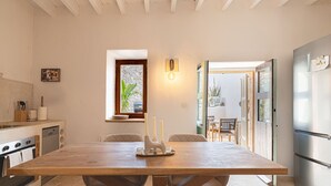A kitchen with a wooden table, a refrigerator, and a window with a plant. - Petra holiday home by Rentallorca (Petra)