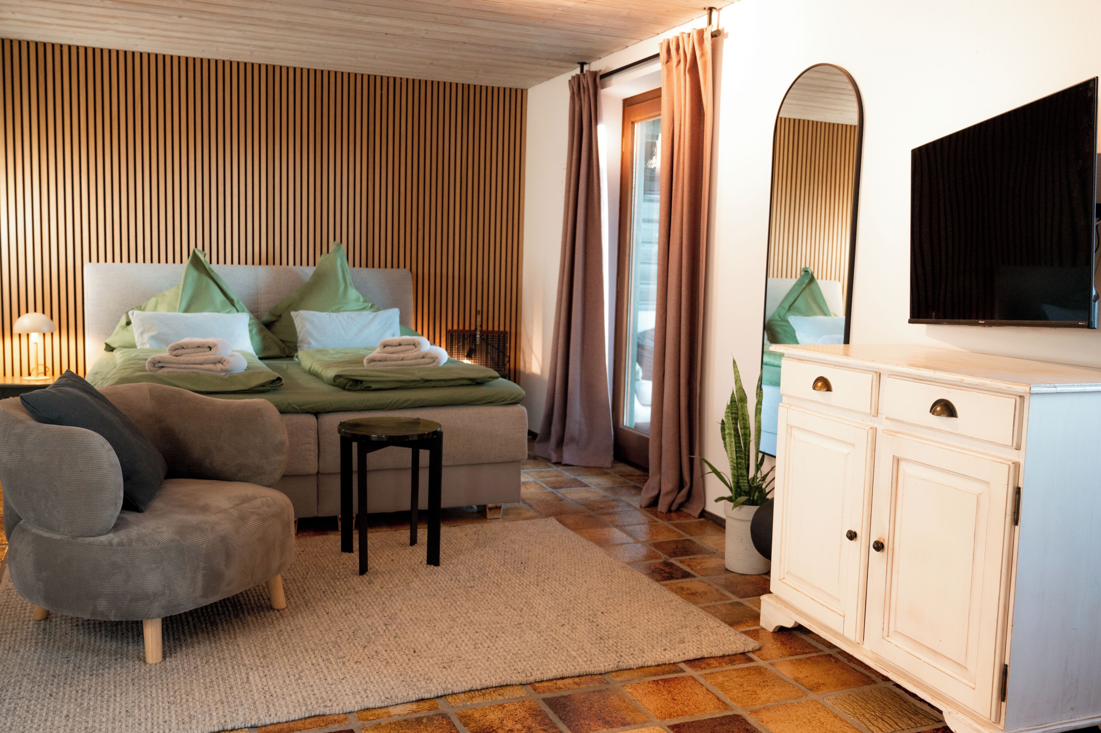 Ein Schlafzimmer mit Bett, Sessel, kleinem Tisch, Fernseher und Schrank.