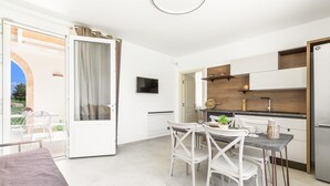 Une cuisine moderne avec des armoires blanches, un comptoir noir et un four encastré. On y trouve un coin repas avec une table et des chaises, ainsi qu’une grande fenêtre donnant sur un jardin.