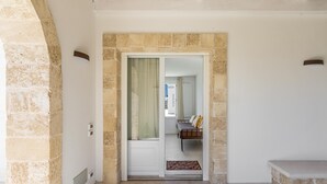 Un couloir aux murs de pierre, une porte blanche et un banc.
