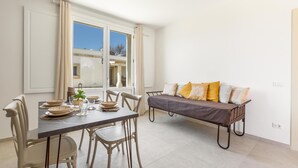 Un coin repas avec une table dressée pour quatre personnes, un canapé avec des coussins et une fenêtre avec des rideaux.