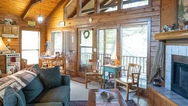 A cozy cabin interior with a wooden ceiling, a fireplace, a dining area, and a living room with a sofa and coffee table. - Heart Shaped Tub for Two, Cabin, Views for miles! (Eureka Springs)