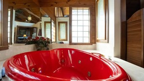 A modern bathroom with a large red bathtub, wooden ceiling beams, and large windows allowing natural light. - Heart Shaped Tub for Two, Cabin, Views for miles! (Eureka Springs)