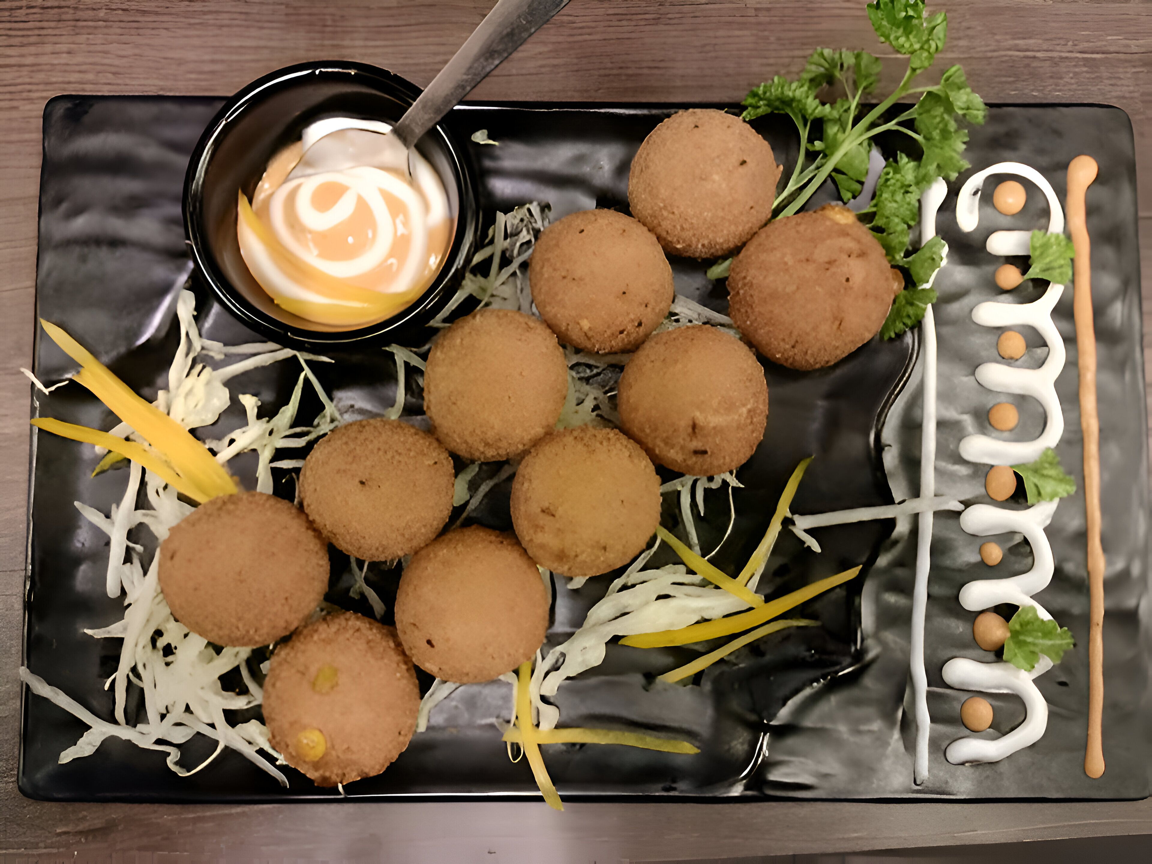 Un plato negro con croquetas, verduras ralladas y salsa para mojar.