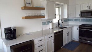 Una cocina moderna con armarios blancos, horno empotrado, microondas y cafetera.