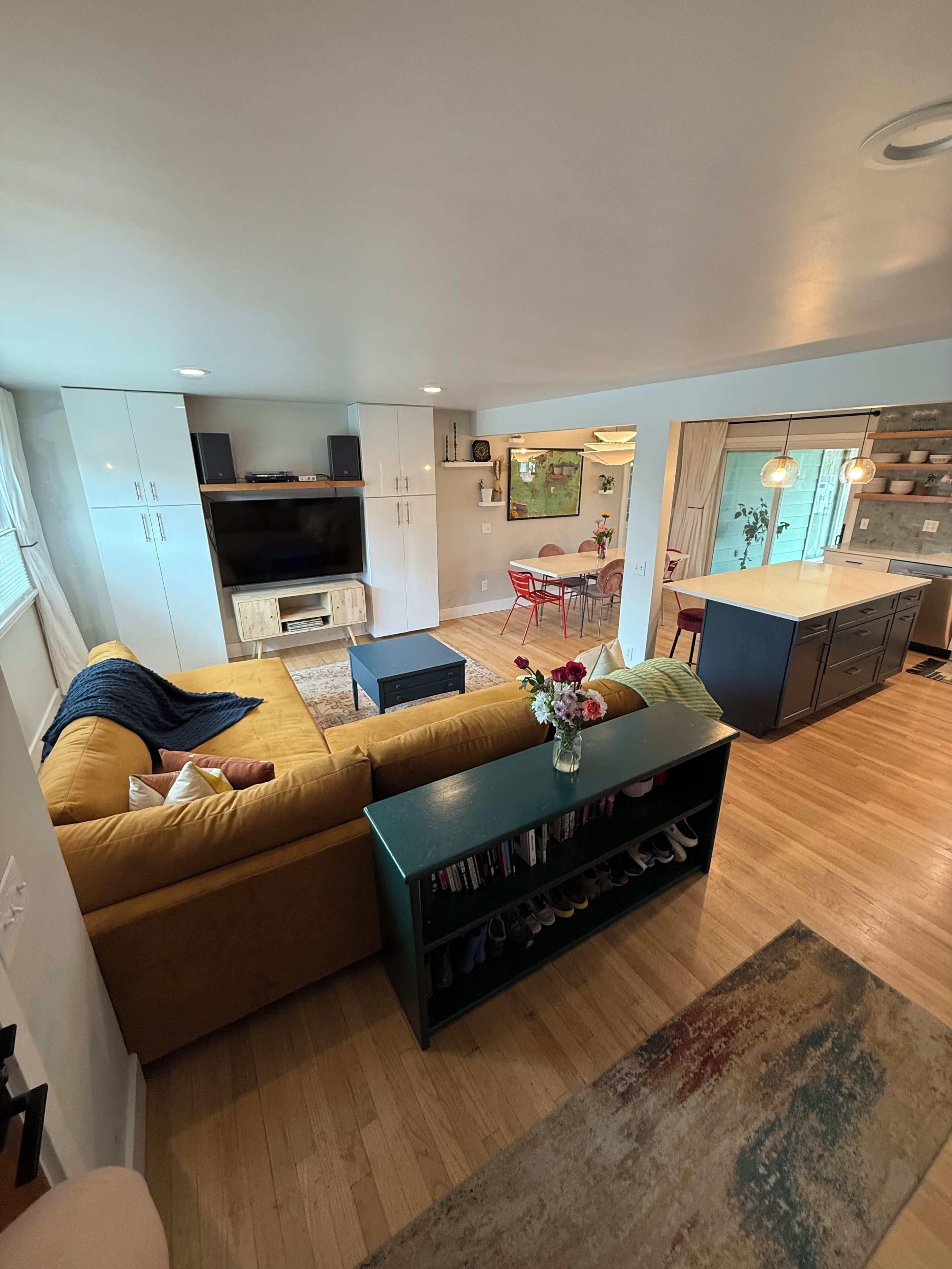 A modern living room with a sofa, coffee table, and a TV. There is a kitchen area with a dining table and chairs.