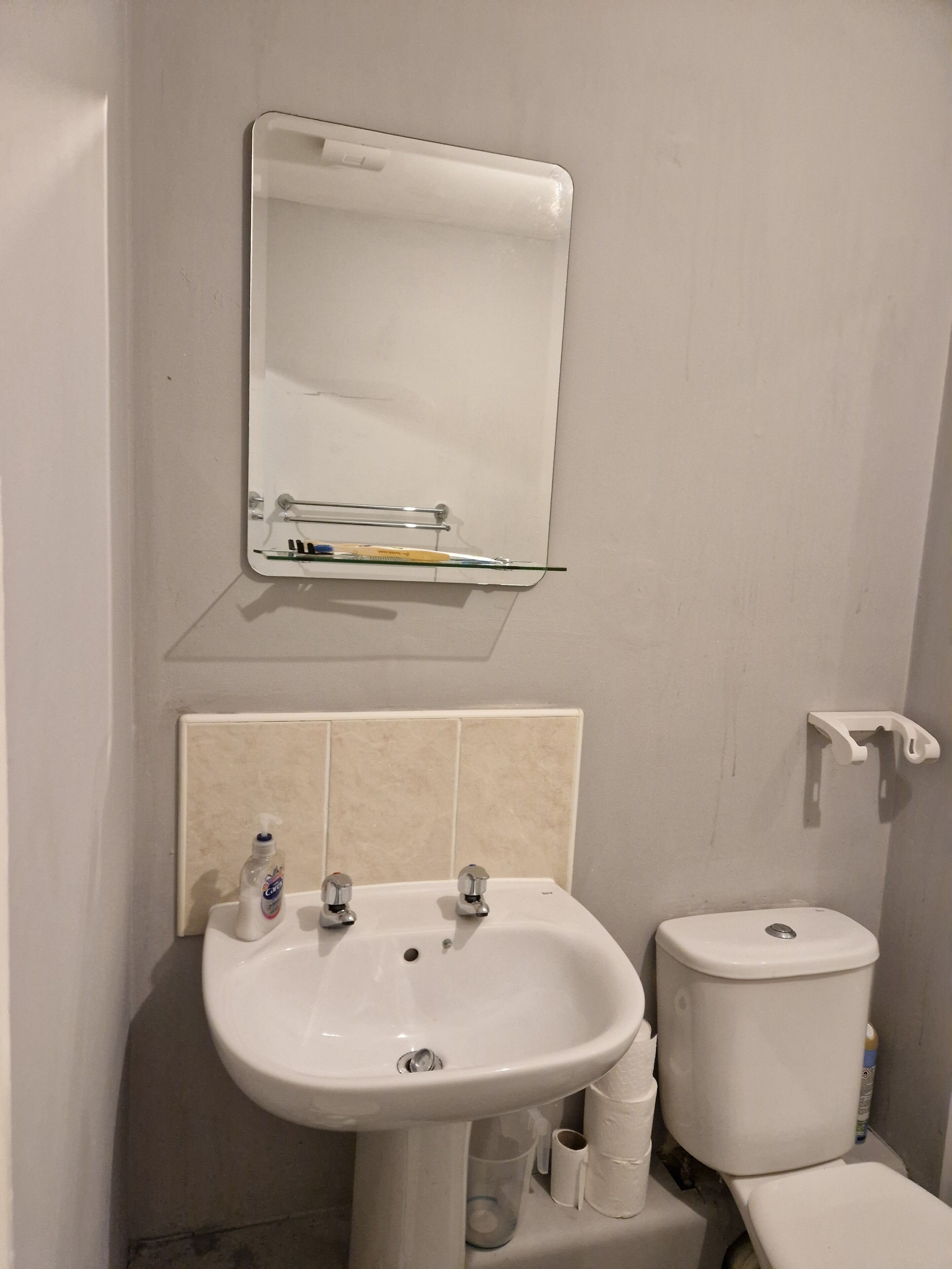 A bathroom with a white sink, two faucets, a mirror, and a toilet.