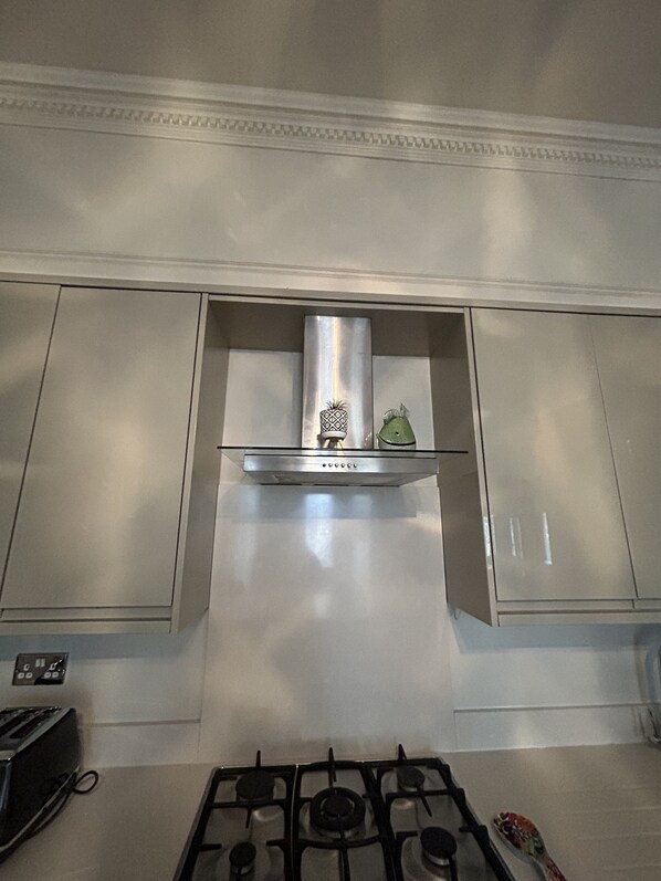 A kitchen with a gas stove, a stainless steel range hood, and white cabinetry.