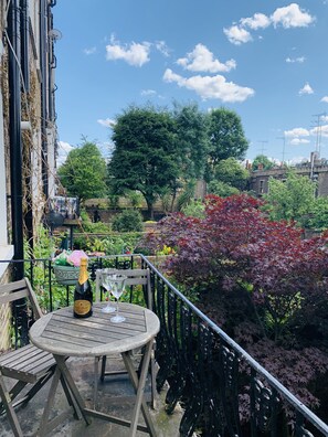 A wooden table with a bottle of champagne and a glass on a balcony.