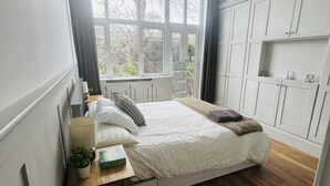 A bedroom with a bed, a bedside table with a lamp, a potted plant, and a window with curtains.