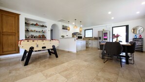 A spacious living area with a foosball table, a kitchen with a bar area, and a dining table with chairs. - Magnifique Villa avec Piscine/Jacuzzi tout confort (Nans-les-Pins)
