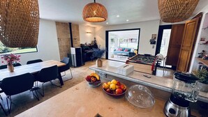 A modern kitchen with a central island, a dining area with a table and chairs, and a visible foosball table in the background. - Magnifique Villa avec Piscine/Jacuzzi tout confort (Nans-les-Pins)