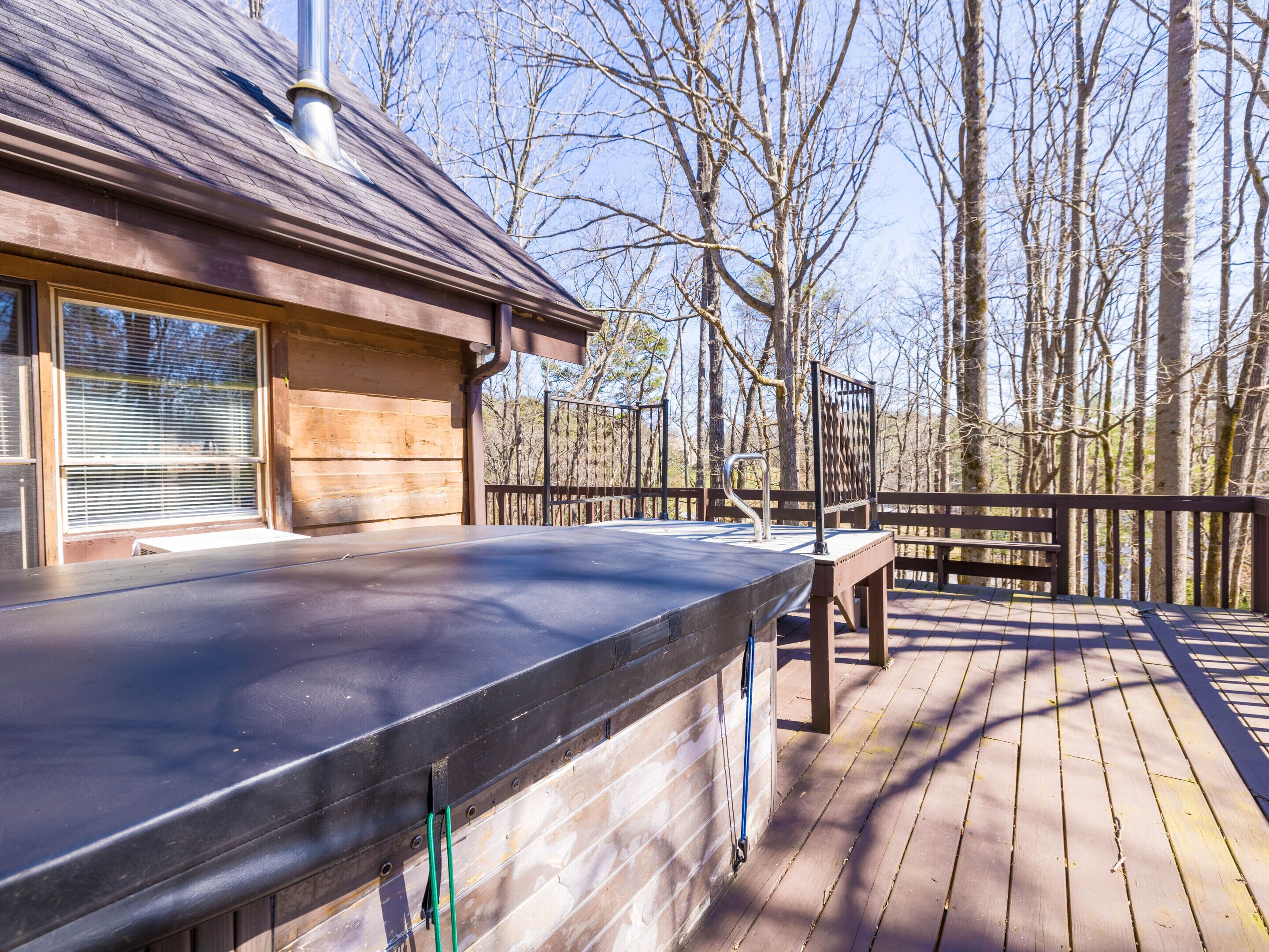 A wooden deck with a metal railing, a bench, and a grill area.