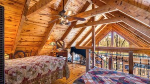 A cozy attic bedroom with wooden beams, a ceiling fan, and two beds with quilts.