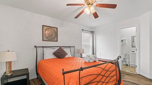 A bedroom with a bed, a ceiling fan, a nightstand, a lamp, and a window with blinds.