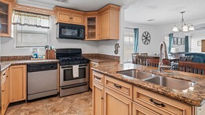 A kitchen with granite countertops, wooden cabinets, stainless steel appliances, and a large island with a sink.