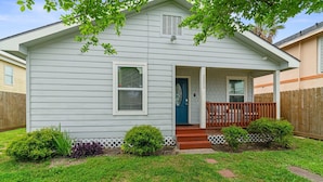 A single-story house with a front porch, a blue door, and a small garden area with shrubs and stepping stones.