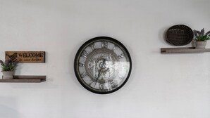 A wall clock with a mechanical design, a welcome sign, and a small shelf with a potted plant.