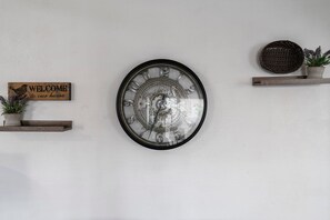 A wall clock with a mechanical design, a welcome sign, and a small shelf with a potted plant.