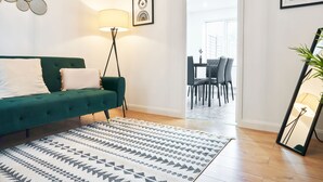 Ein modernes Wohnzimmer mit einem grünen Sofa, einem gemusterten Teppich und einer Stehlampe.