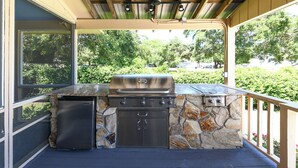 An outdoor kitchen with a built-in grill, a refrigerator, and stone accents. - Gorgeous Inlet View Pet Friendly 3 BR Home with a Private Pool! Kohler's Cottage (Murrells Inlet)