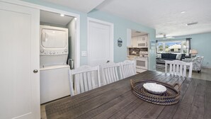 A laundry area with a washer and dryer, a dining table with a woven basket, and a view of the kitchen and living area.