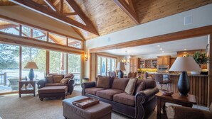 Ein geräumiges Wohnzimmer mit einer großen Holzbalkendecke, einem gemütlichen braunen Sofa und einem Essbereich mit Holzschränken sowie einer Küche im Hintergrund.
