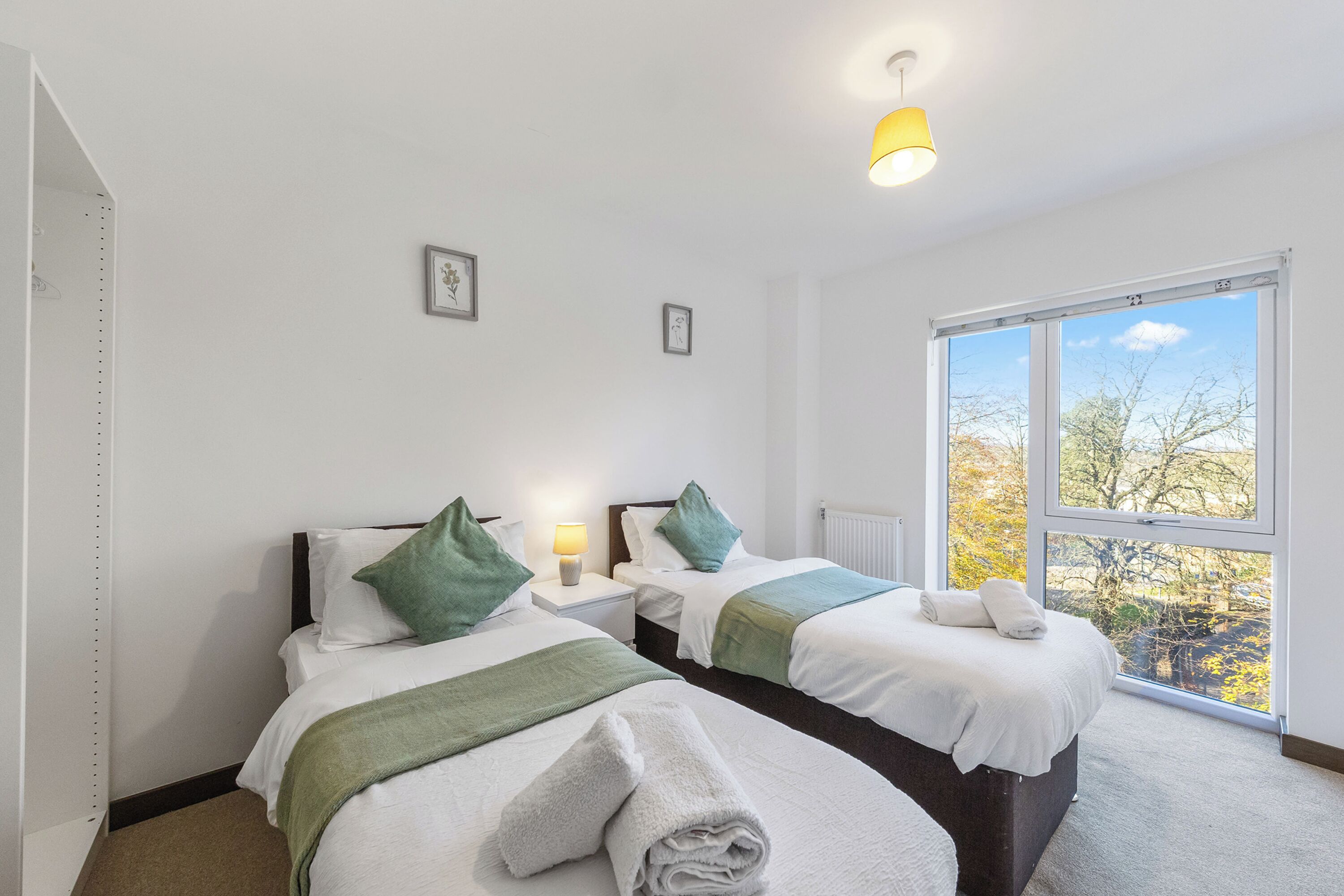 Ein Hotelzimmer mit zwei Betten, einem großen Fenster mit Blick, einem Nachttisch mit Lampe und einer Deckenleuchte.