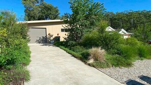 A residential property with a concrete driveway leading to a garage, surrounded by lush greenery and trees.