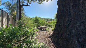 Un espace pique-nique équipé d’une table et de bancs, entouré d’arbres et d’une clôture en bois.