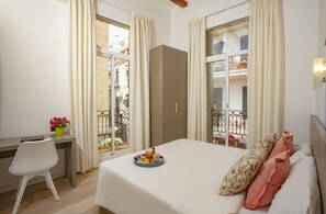 A bedroom with a bed, a desk, and a window with curtains. - Antonios Hostal (Sitges)