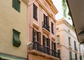 A pink building with black shutters and a balcony with potted plants. - Antonios Hostal (Sitges)