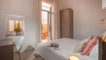 Une chambre à coucher comprenant un lit, un bureau, une chaise, une fenêtre avec des rideaux et donnant sur un balcon extérieur.