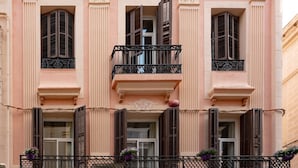 A pink building with three balconies, each with a wrought iron railing and potted plants. - Antonios Hostal (Sitges)