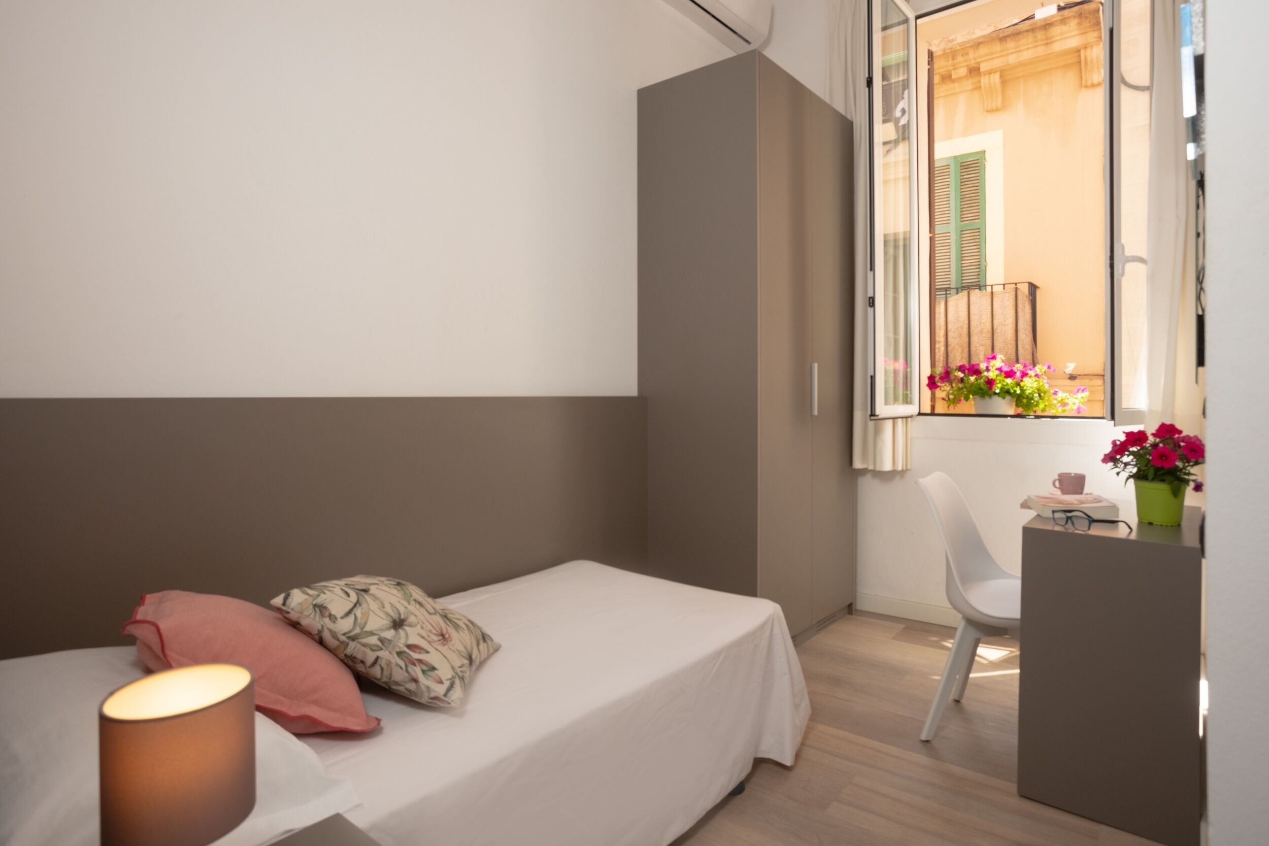 Un dormitorio pequeño con una cama individual, una mesita de noche, una silla y una ventana con vistas al balcón.