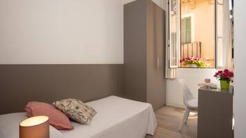 Un dormitorio pequeño con una cama individual, una mesita de noche, una silla y una ventana con vistas al balcón.