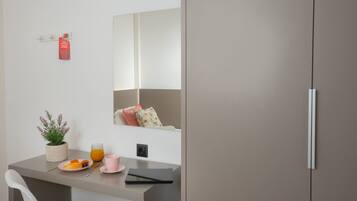 Habitación moderna con un armario gris, una mesita con una planta, un plato de comida, un vaso de jugo de naranja y una taza rosa.