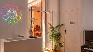 Un intérieur moderne avec un piano, un néon en forme de fleur et une porte portant le numéro 105.