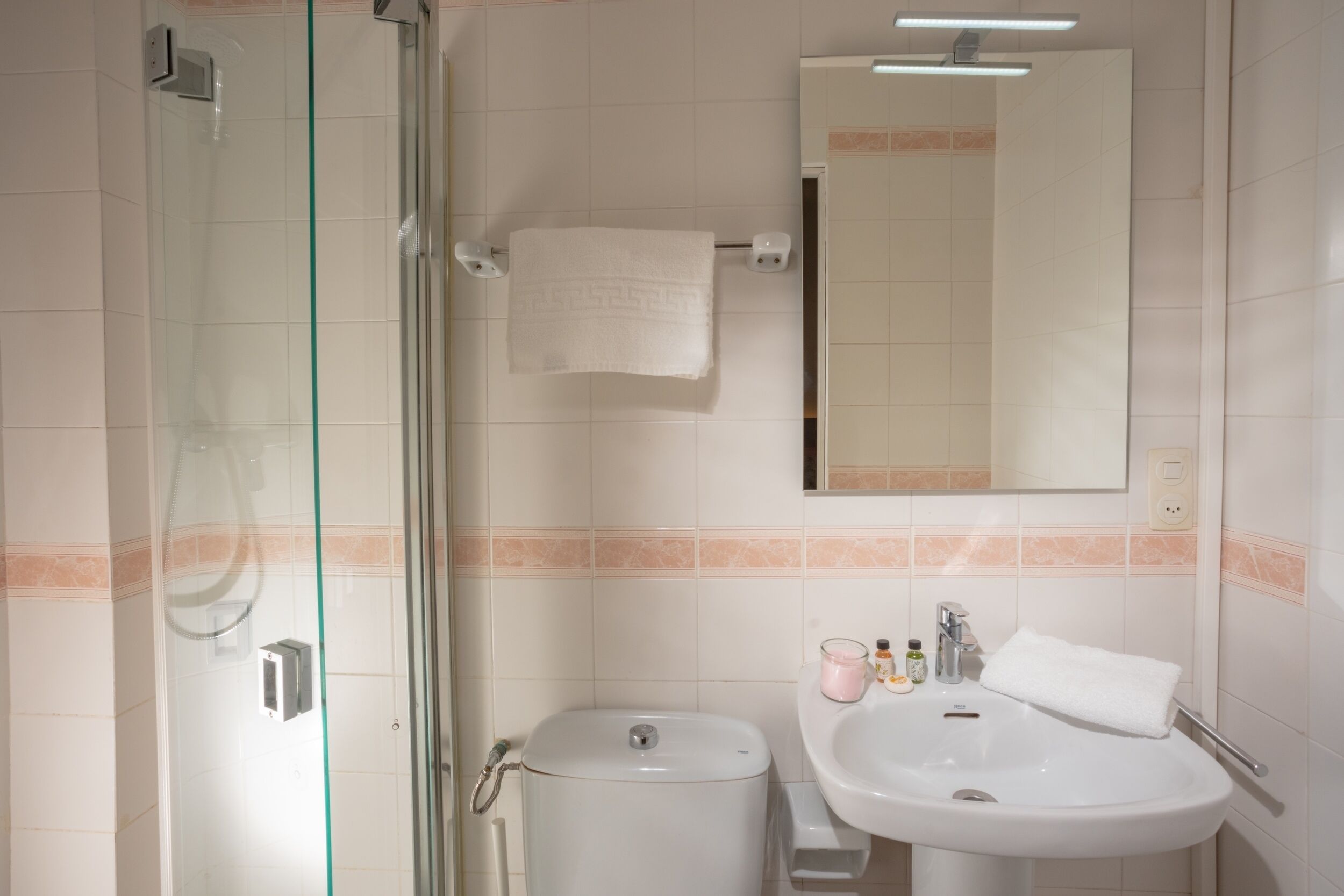 Un baño con cabina de ducha de vidrio, inodoro, lavamanos con espejo y una toalla colgada en la pared.