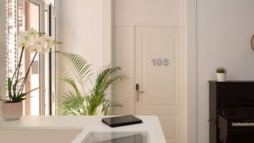 A room with a piano, a door with the number 105, a tablet on a table, and potted plants.