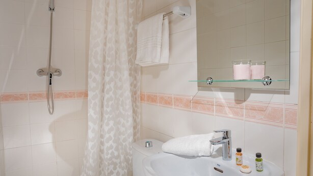 A bathroom with a shower, toilet, sink, and a mirror with a glass shelf above it. - Antonios Hostal (Sitges)