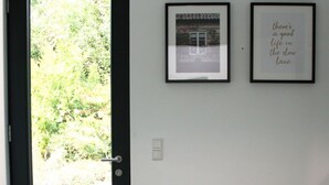 Une pièce avec une porte noire, un banc, deux tableaux encadrés et un interrupteur sur le mur.