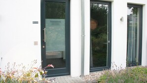 Un bâtiment à la façade blanche, doté de deux portes vitrées et d’un petit jardin agrémenté de plantes de lavande.