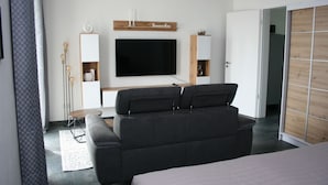 Une chambre moderne avec un canapé noir, un téléviseur à écran plat et un meuble en bois.