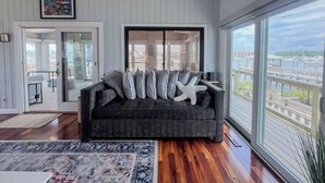Een moderne woonkamer met een donkergrijze bank, een groot raam met uitzicht over de stad, en een ingelijste foto aan de muur.