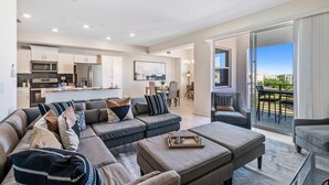 A modern living room with a sectional sofa, a glass coffee table, and a view of the city through large windows. - Pool View 2 bedroom! Close to Disney World! (Kissimmee)
